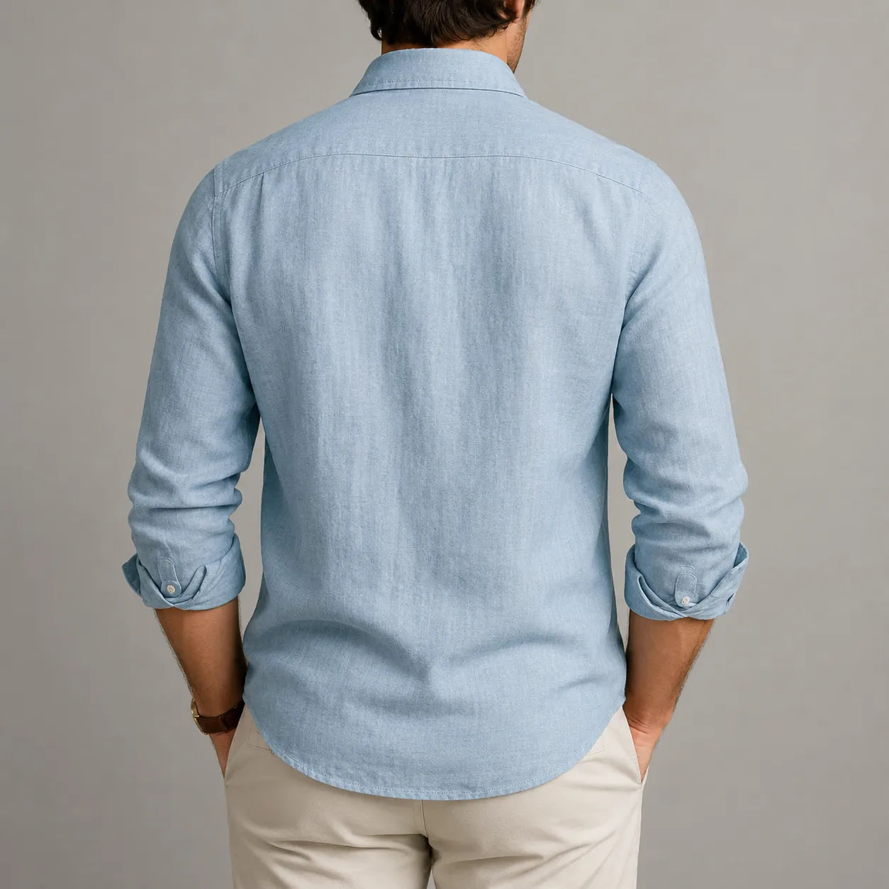 Person wearing a light blue denim shirt with rolled-up sleeves on a gray background